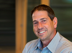 Joel West - website A man smiling for the camera in front of a building.