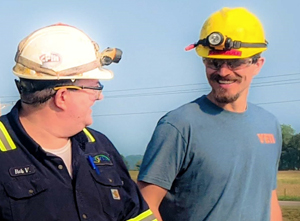 Two men in hard hats and safety glasses talking.